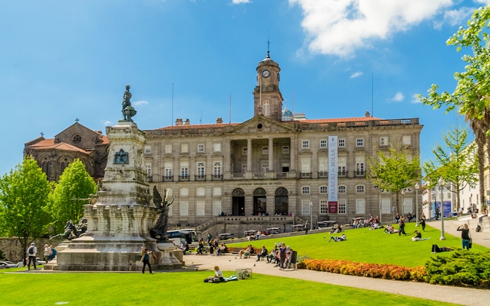 Stock Exchange Palace and Don Henrique Statue in Porto, Portugal, with people relaxing on the lawn.