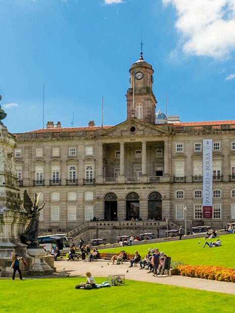 Stock Exchange Palace and Don Henrique Statue in Porto, Portugal, with people relaxing on the lawn.