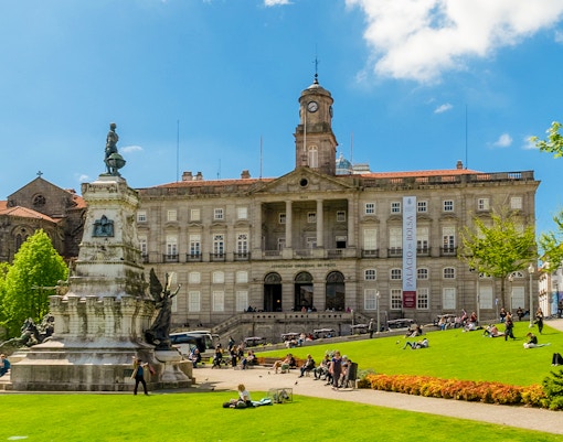 Stock Exchange Palace and Don Henrique Statue in Porto, Portugal, with people relaxing on the lawn.