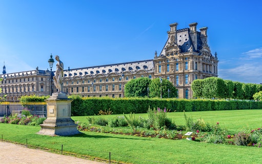 Louvre Museum with Tuileries Garden statue and manicured lawns in Paris.