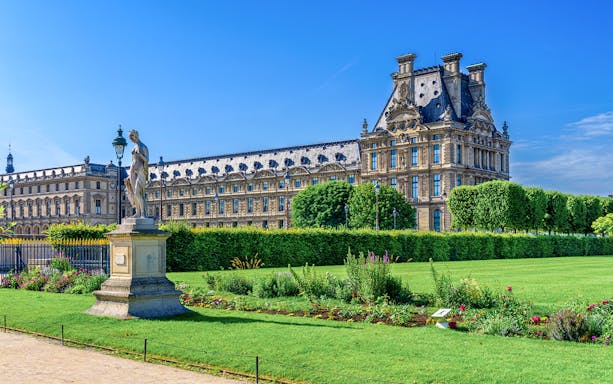 Louvre Museum with Tuileries Garden statue and manicured lawns in Paris.