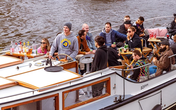 Amsterdam canal cruise with people enjoying drinks and smoking on a boat.