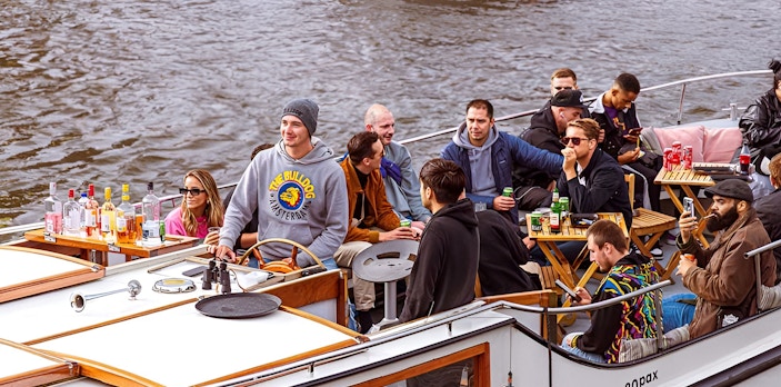 Amsterdam canal cruise with people enjoying drinks and smoking on a boat.