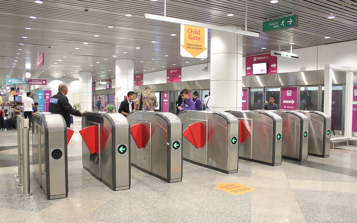 Turnstiles at KLIA Ekspress station, Kuala Lumpur, with passengers passing through.