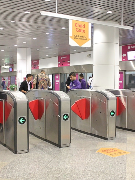 Turnstiles at KLIA Ekspress station, Kuala Lumpur, with passengers passing through.