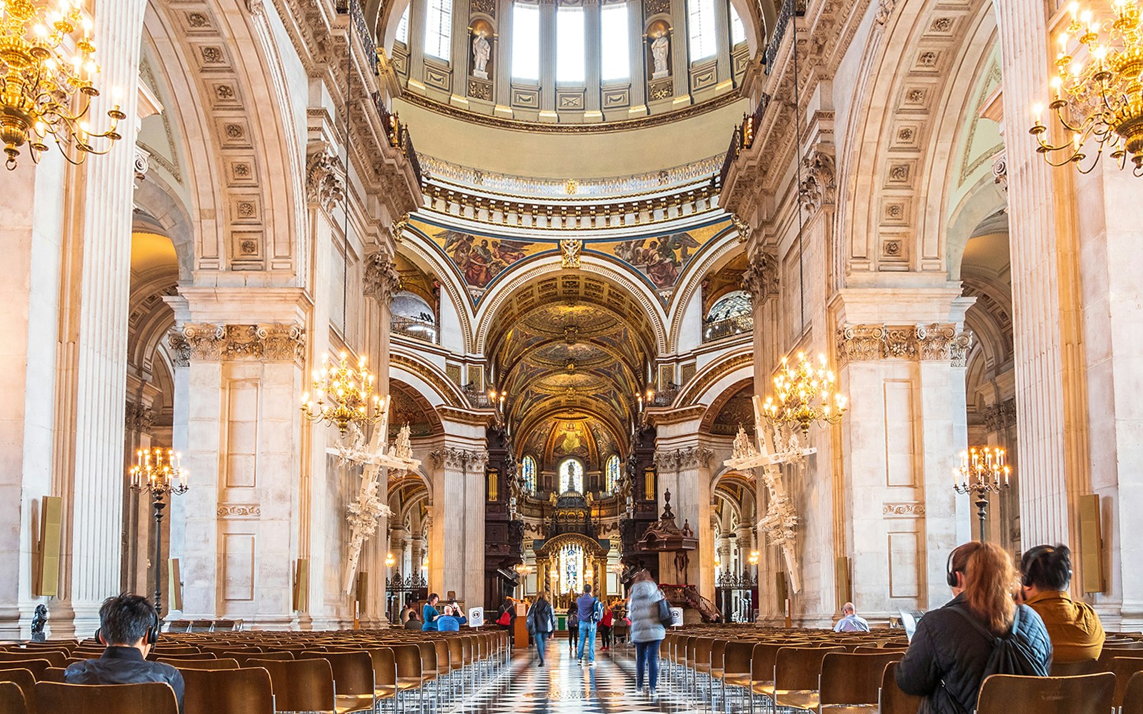 Mehrere Menschen laufen das Kirchenschiff in der mit Kronleuchtern erhellten St. Paul’s Cathedral entlang