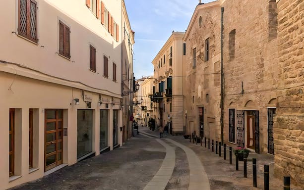 Narrow cobblestone street in Alghero's historic center with stone buildings.
