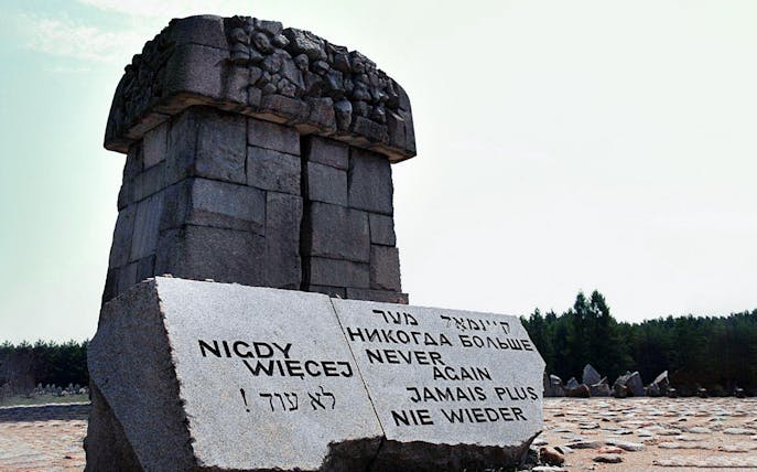 Memorial stone at Treblinka Extermination Camp with "Never Again" in multiple languages.