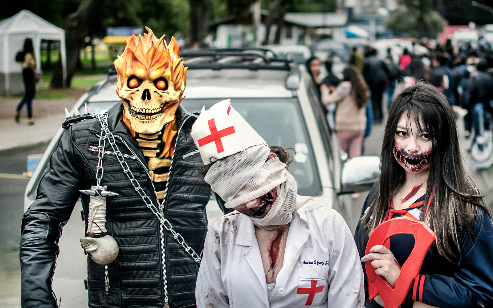 Costumed participants at a Halloween parade with a fiery skull, bandaged nurse, and zombie makeup.