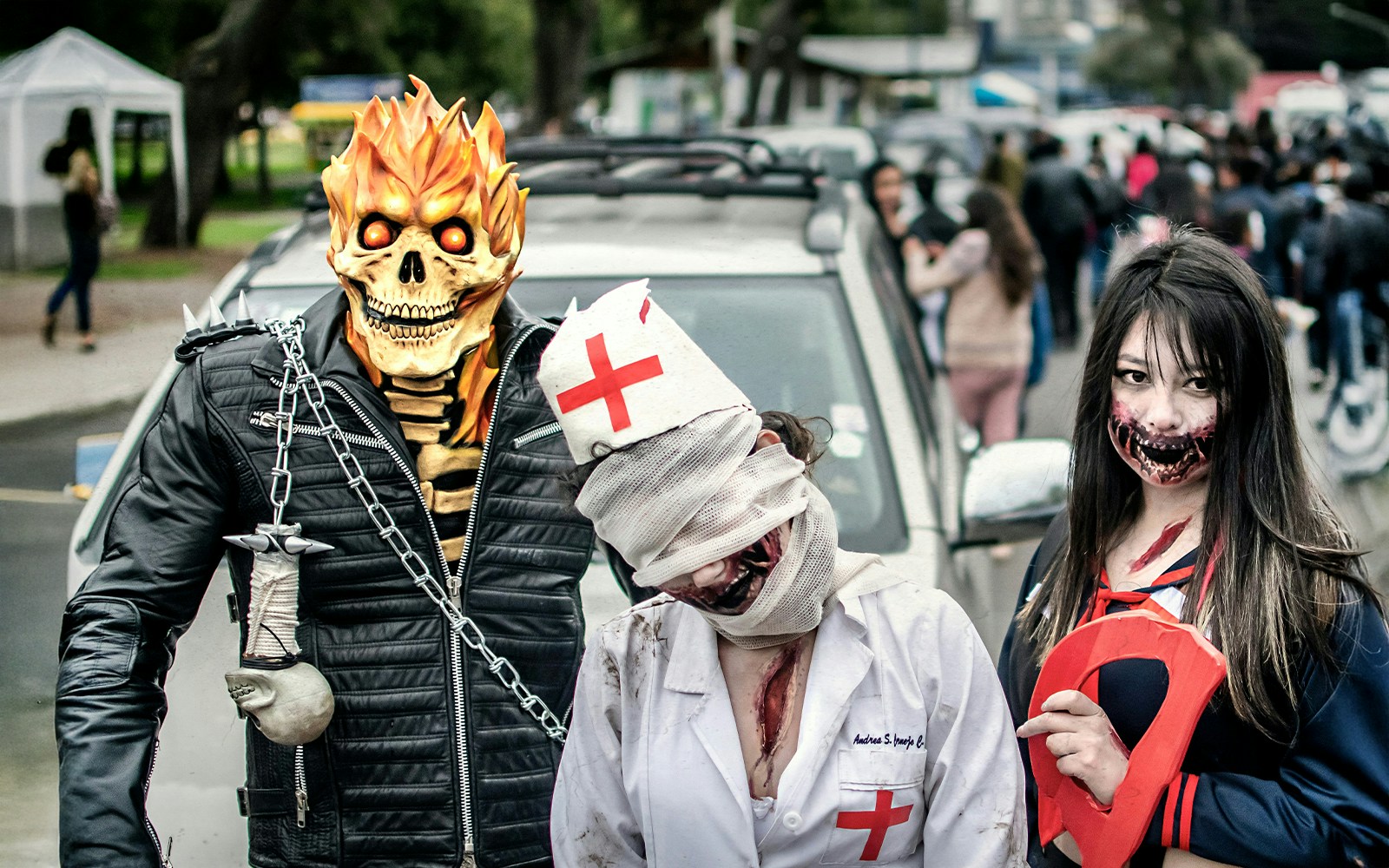 Costumed participants at a Halloween parade with a fiery skull, bandaged nurse, and zombie makeup.