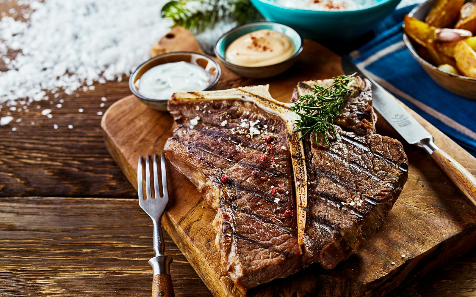 T-bone steak on wooden board with rosemary and garlic cloves.