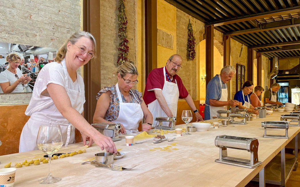 People in Siena cooking class making pasta at a long table with pasta machines.