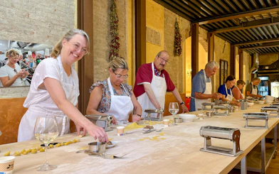 People in Siena cooking class making pasta at a long table with pasta machines.