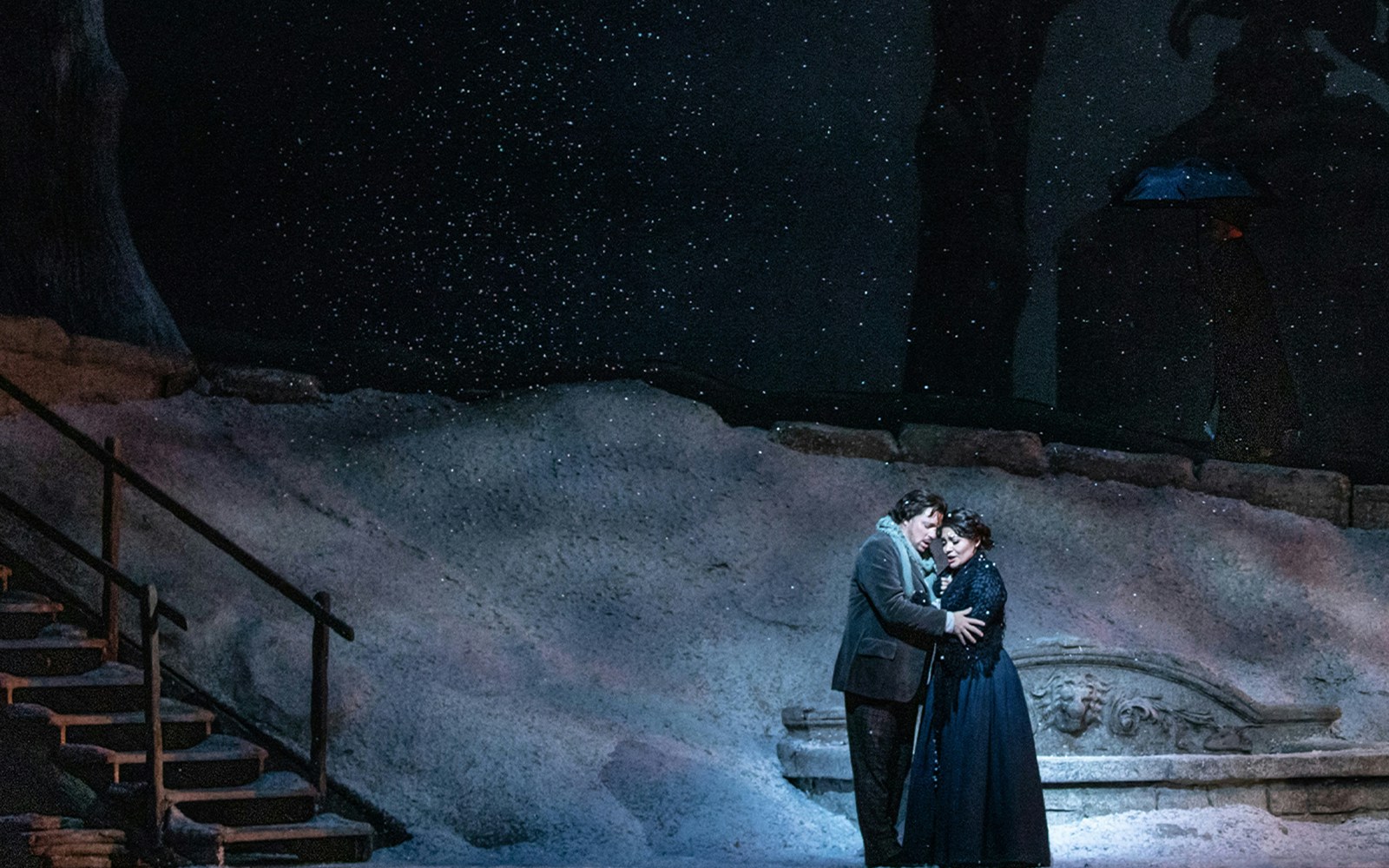 Couple embracing on snowy stage during La Boheme performance.