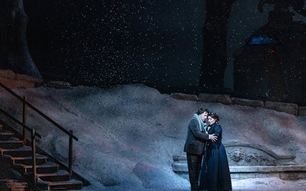 Couple embracing on snowy stage during La Boheme performance.