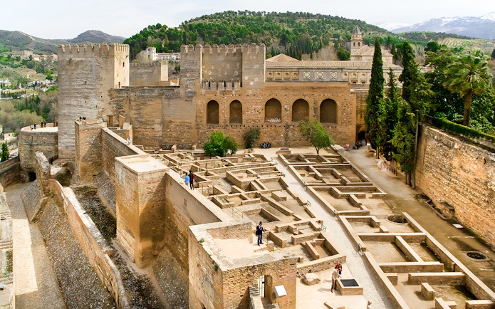 Alhambra fortress walls and ruins in Granada, Spain, with surrounding hills.