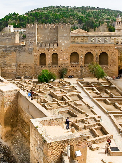 Alhambra fortress walls and ruins in Granada, Spain, with surrounding hills.