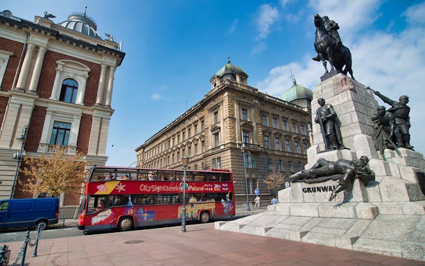 Krakow hop-on hop-off bus near Grunwald Monument and historic buildings.