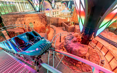 Roller coaster track inside Doha Quest Theme Park with vibrant lights and rocky landscape.