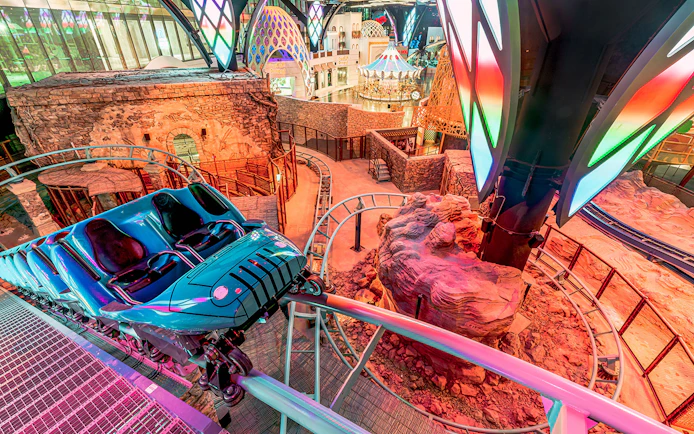 Roller coaster track inside Doha Quest Theme Park with vibrant lights and rocky landscape.
