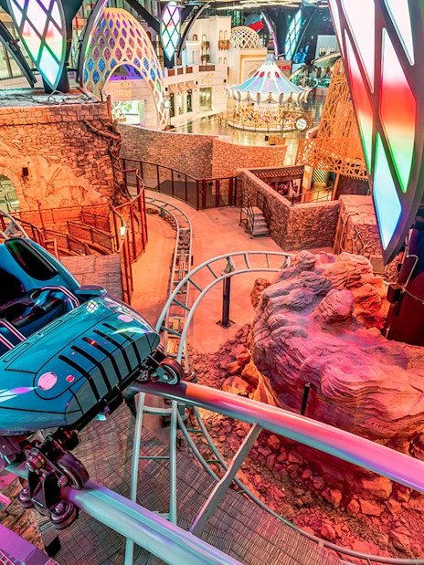 Roller coaster track inside Doha Quest Theme Park with vibrant lights and rocky landscape.