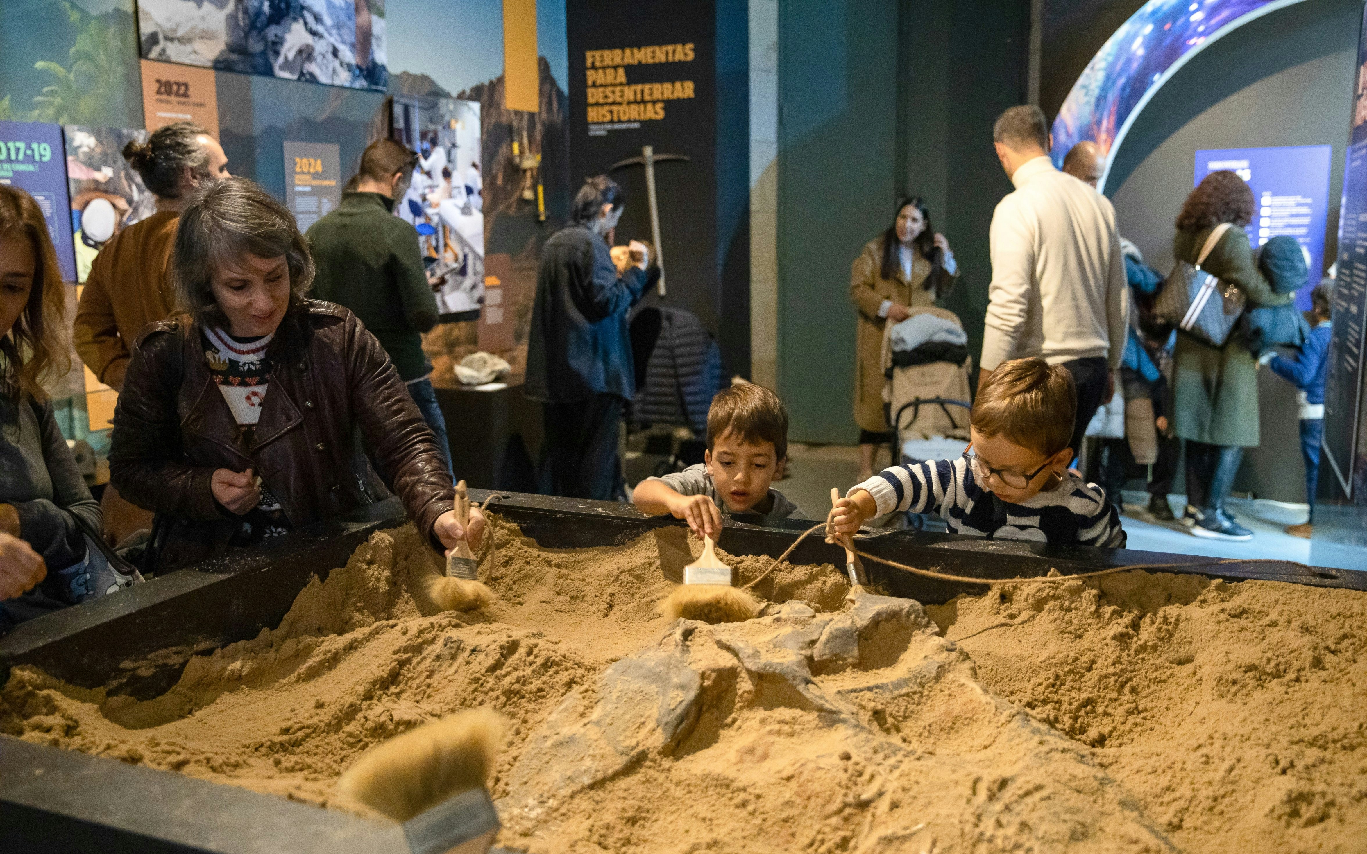 Children exploring dinosaur fossils at Dino Experience Porto exhibition.