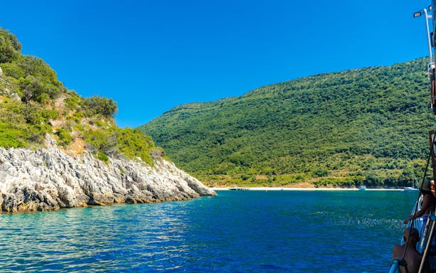 Kakome beach coastline with lush green hills and clear blue water, viewed from a boat.