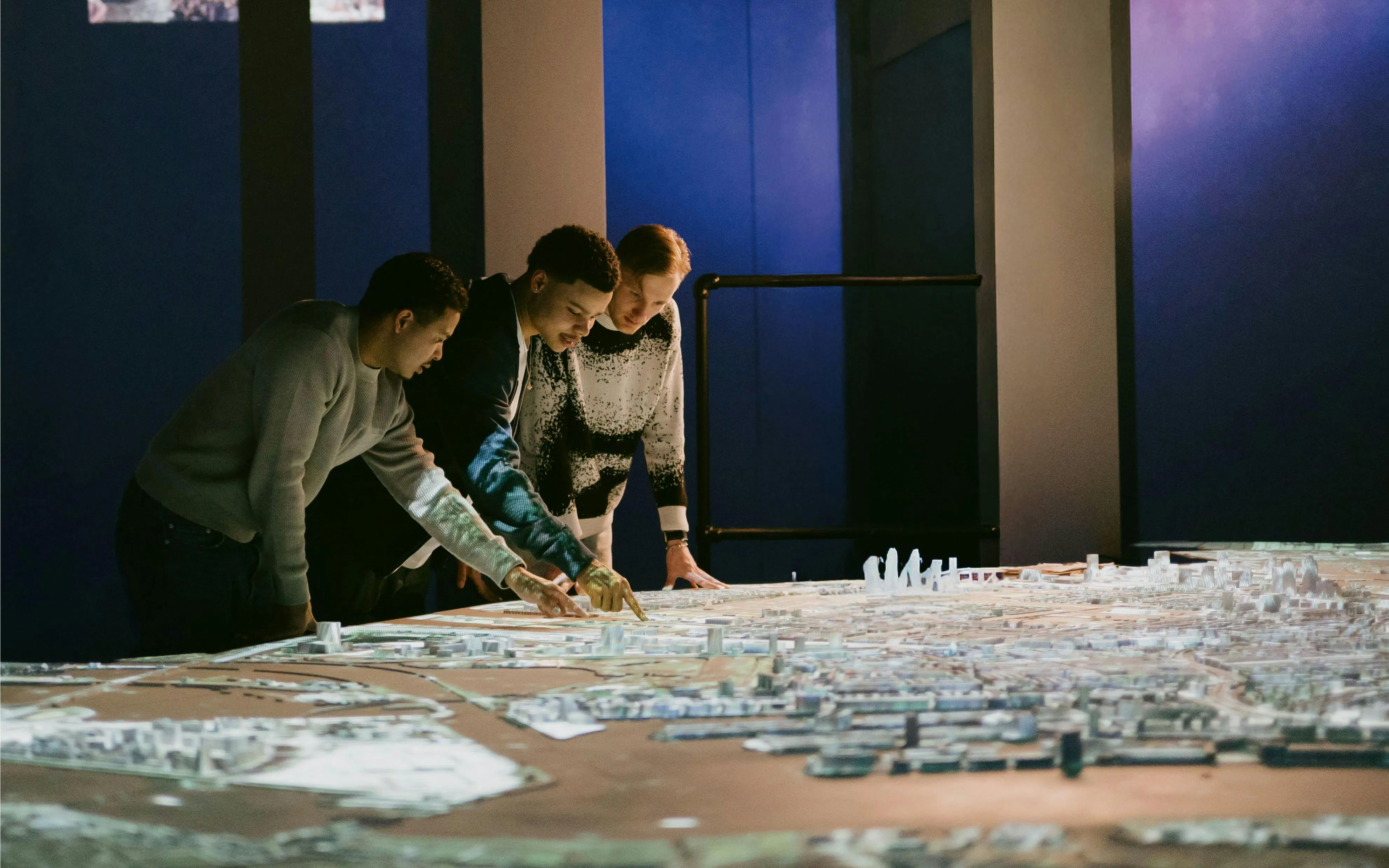 People examining a detailed model of Amsterdam in a dimly lit exhibit.