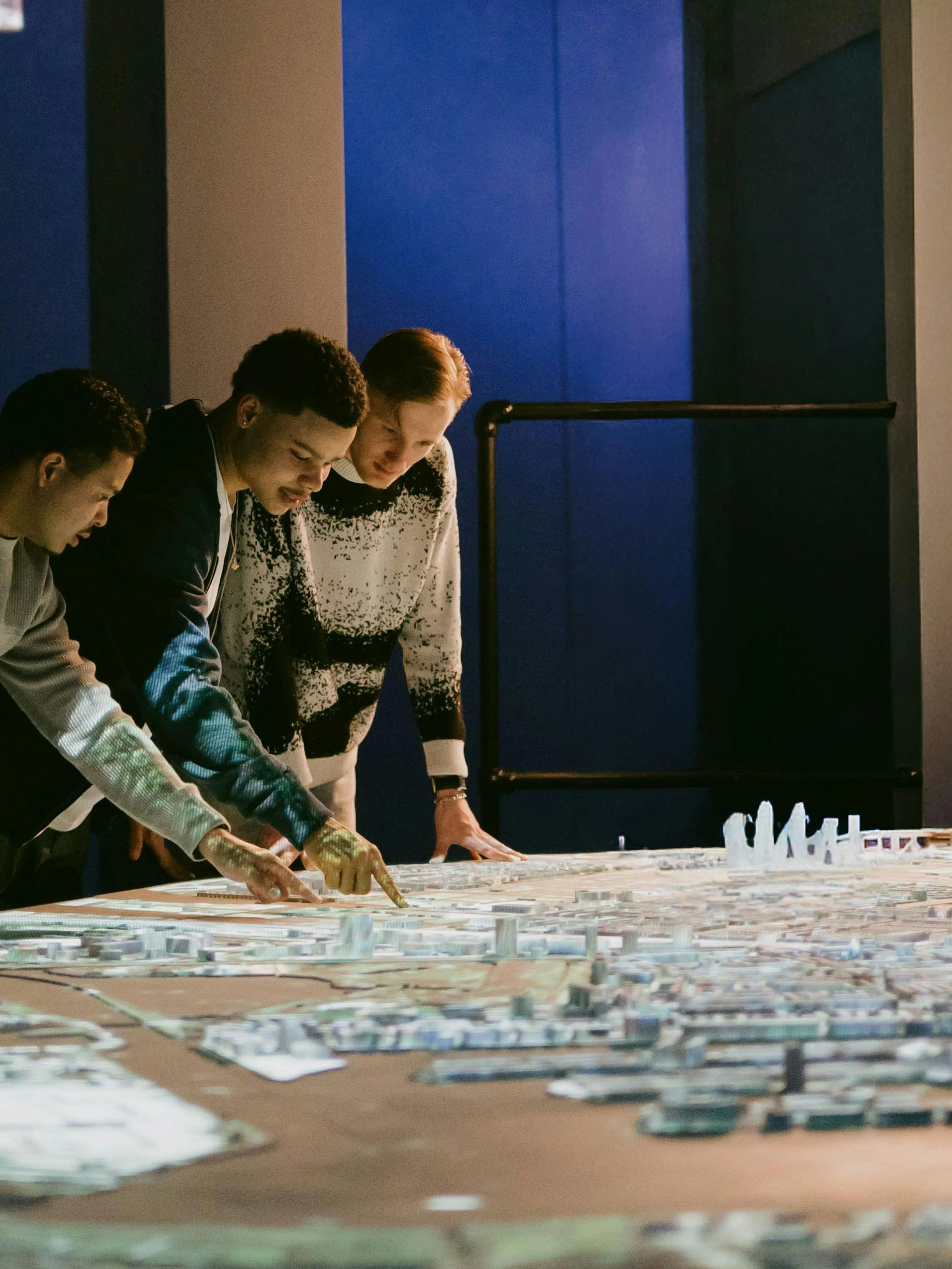 People examining a detailed model of Amsterdam in a dimly lit exhibit.