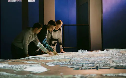 People examining a detailed model of Amsterdam in a dimly lit exhibit.