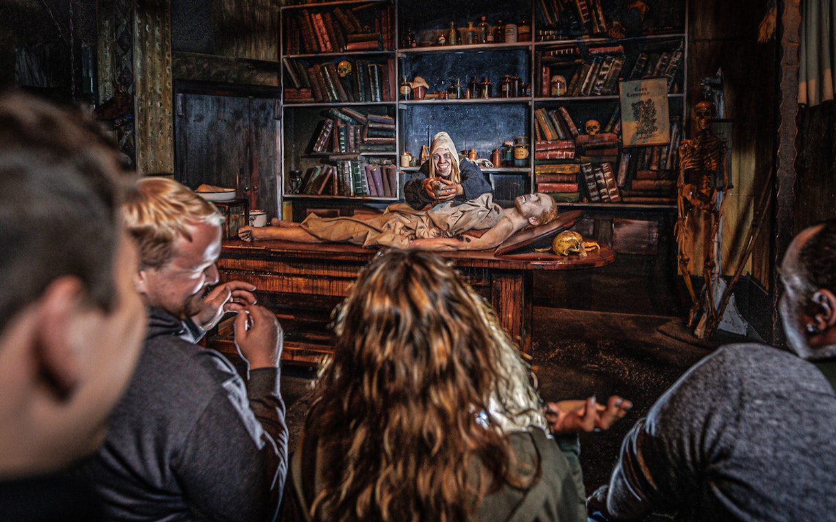 Audience watching Plague act in Hamburg Dungeon with actor and patient on table.