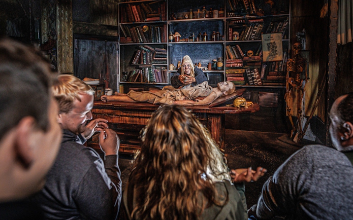 Audience watching Plague act in Hamburg Dungeon with actor and patient on table.