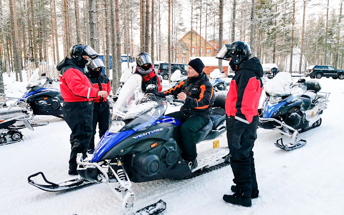 Group preparing for snowmobile tour in Rovaniemi forest.