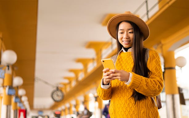 Asian woman using smartphone at a bus station.