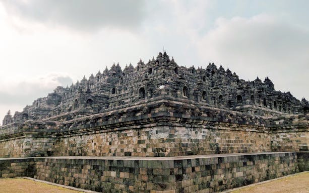 Borobudur Temple stone structure under cloudy sky, Indonesia.