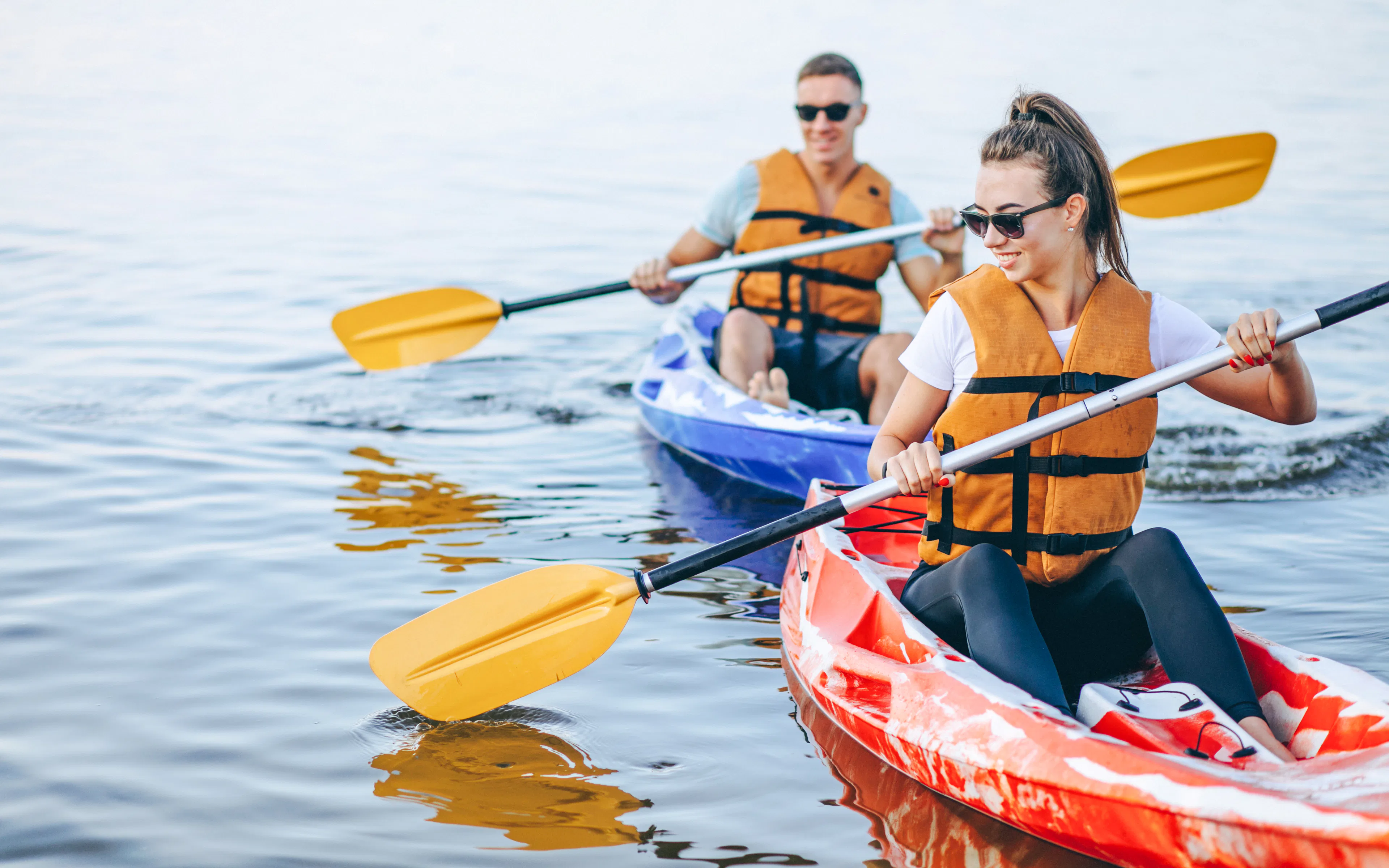 Couple kayaking on a river in tandem, wearing life vests and sunglasses.