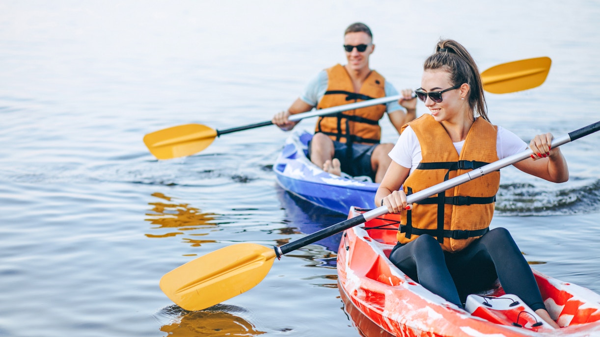 Couple kayaking on a river in tandem, wearing life vests and sunglasses.