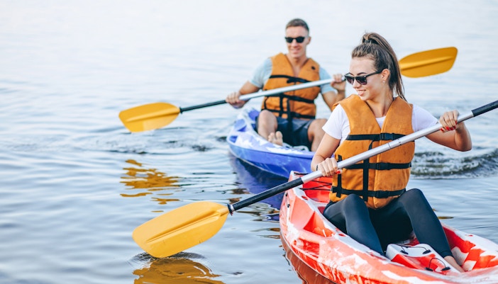 Couple kayaking, wearing life vests and sunglasses.