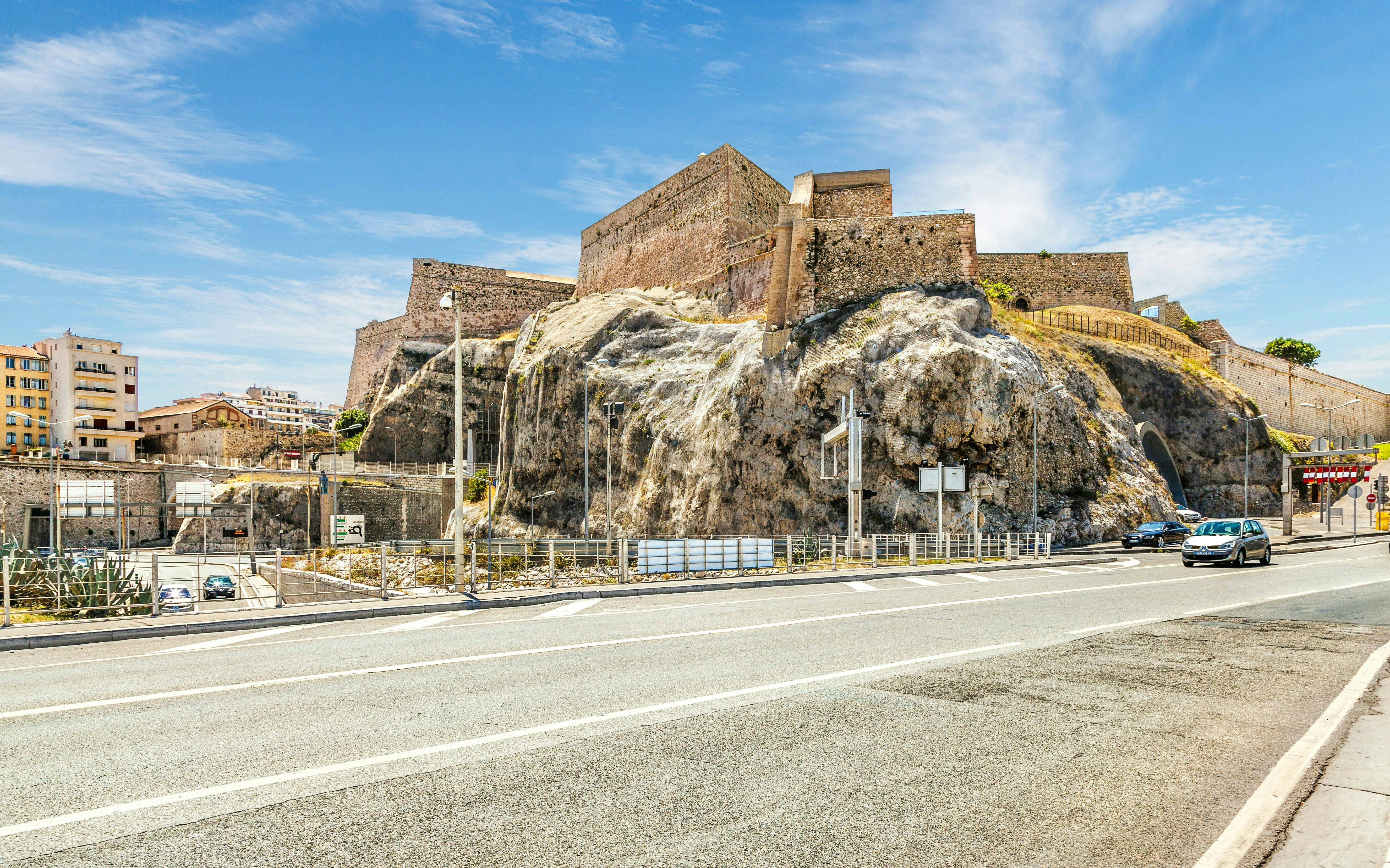 Fort Nicolas in Marseille, France, with stone walls and rocky base along a city road.