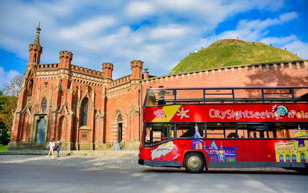 Krakow hop-on hop-off bus near Kościuszko Mound and historic brick building.