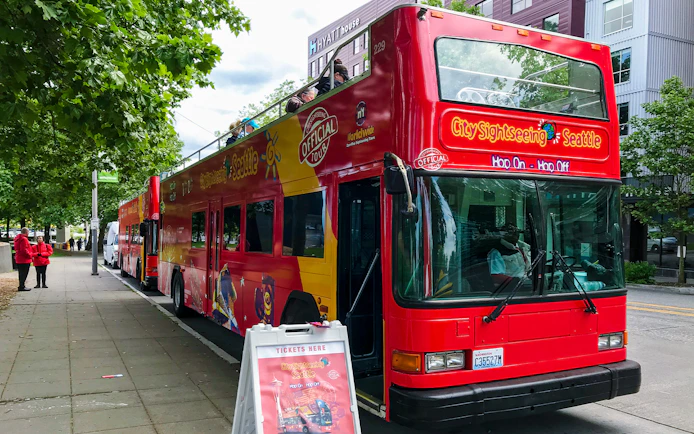 Red double-decker tour bus parked in Seattle street with ticket sign nearby.