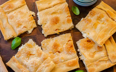 Focaccia di Recco slices on a wooden board during a Genoese cooking lesson in Genoa.