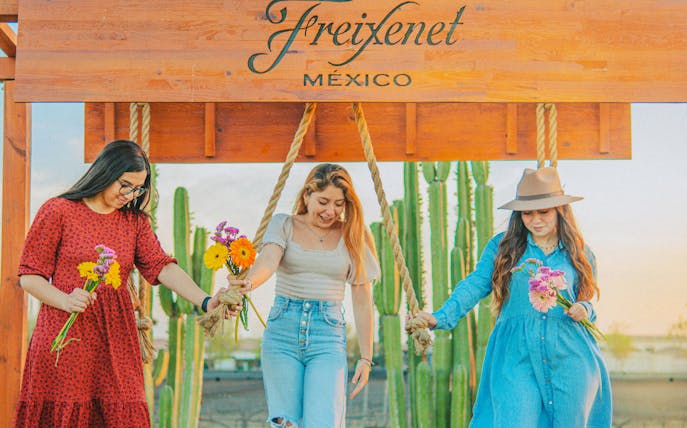 Women holding flowers at Freixenet Mexico vineyard, Queretaro, with cacti in the background.