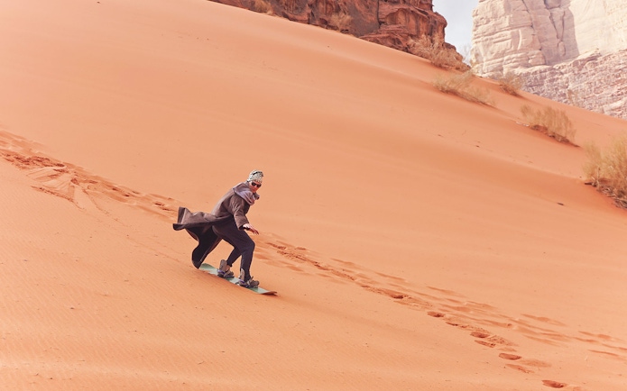 Person sandboarding down a desert dune during a private group safari experience.