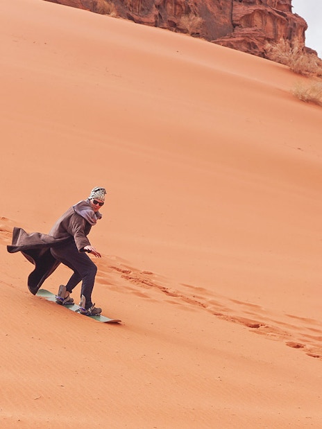 Person sandboarding down a desert dune during a private group safari experience.