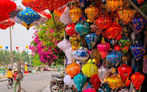 Colorful lanterns hanging in Hoi An street, Da Nang, with vibrant flowers and a cyclist nearby.