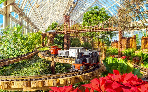 Model trains on tracks with festive decorations at New York Botanical Gardens.