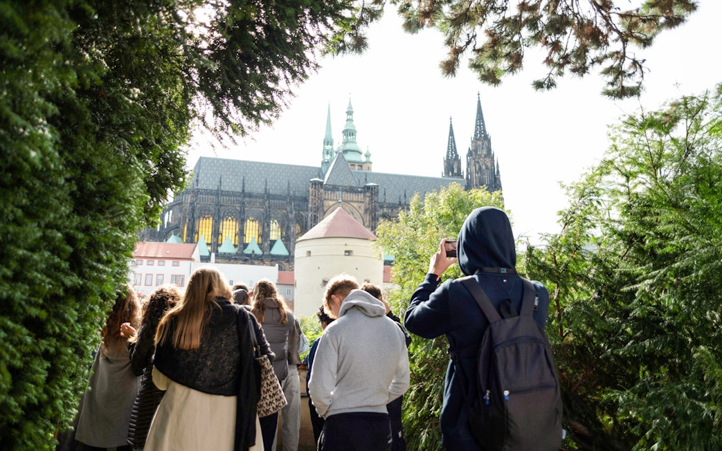 Group touring Prague Castle grounds with view of cathedral spires.