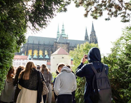 Group touring Prague Castle grounds with view of cathedral spires.