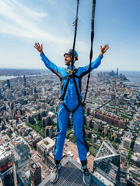 Person harnessed on skyscraper edge overlooking New York City skyline.